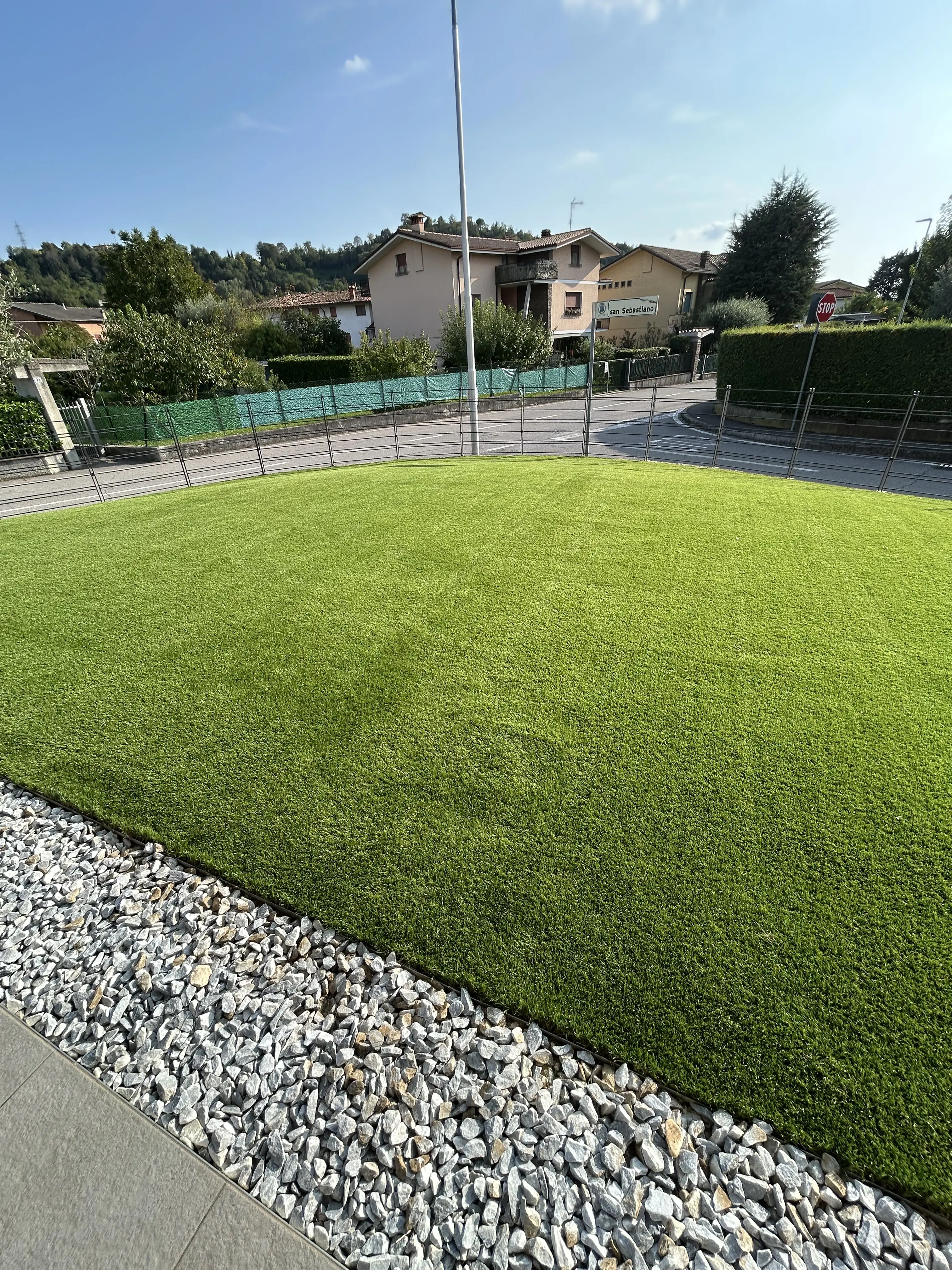 Ampio prato verde naturale curato con bordura in sassi bianchi decorativi.