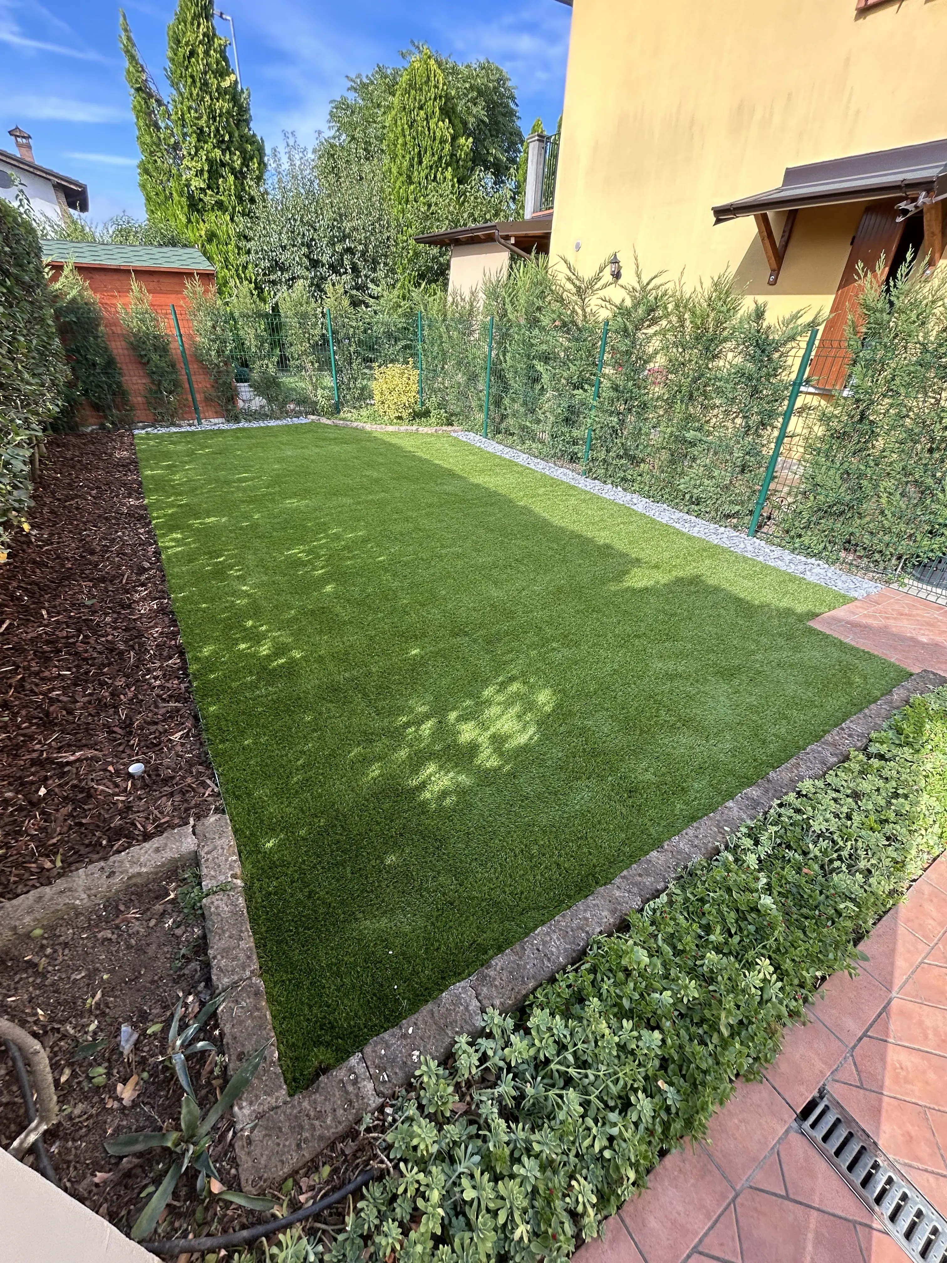 Manutenzione giardino con bordure in corteccia e installazione erba artificiale.