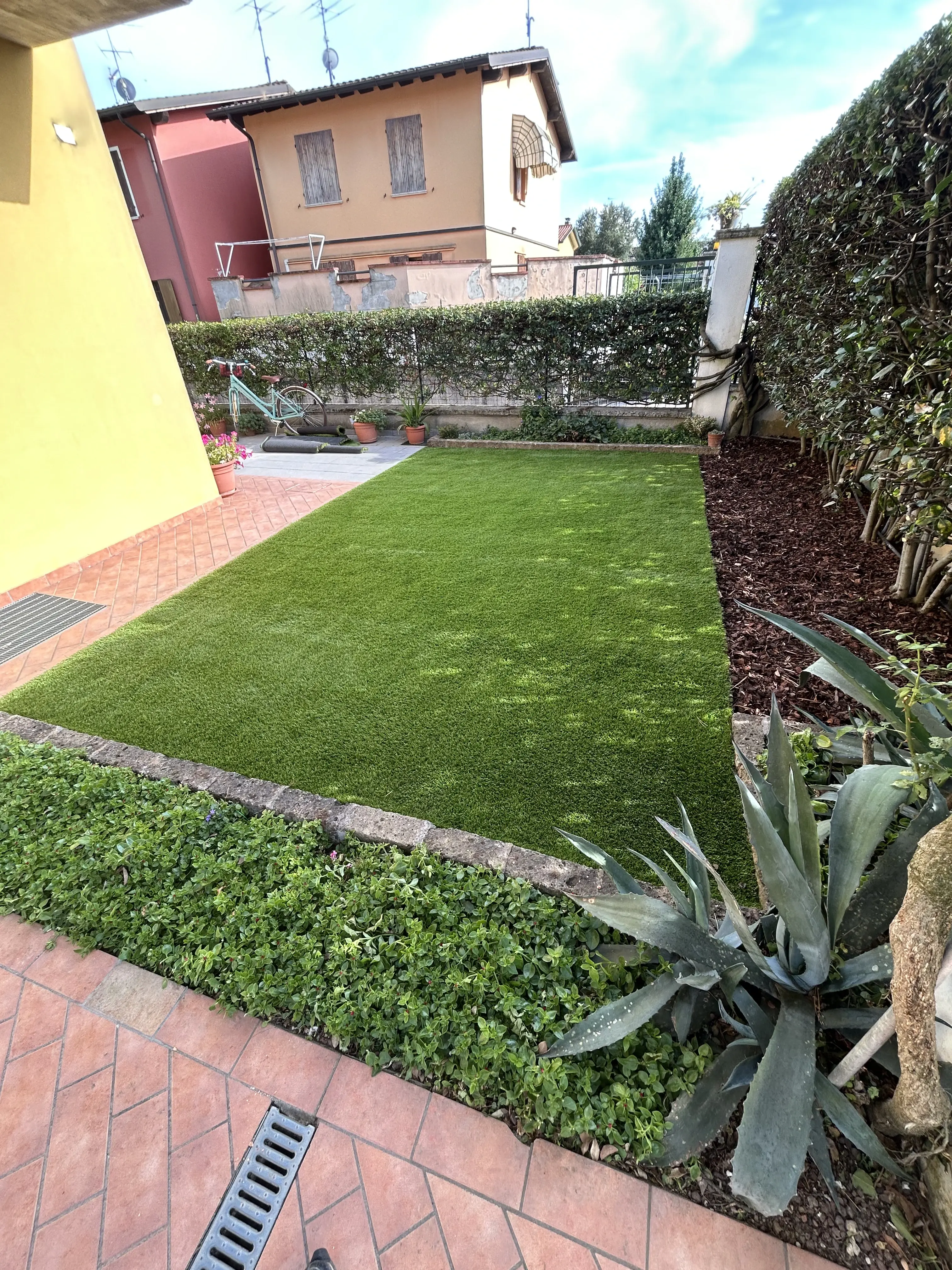 Piccolo giardino domestico trasformato con prato sintetico e aiuole di piante grasse.
