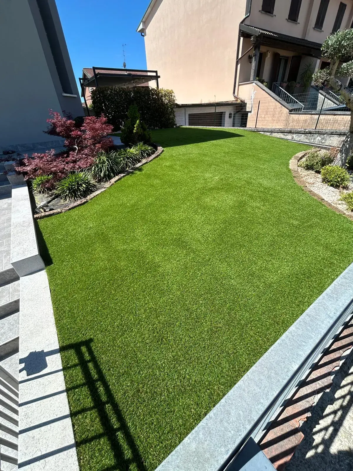 Area verde esterna con prato sintetico, divanetti e siepi perimetrali a Brescia.